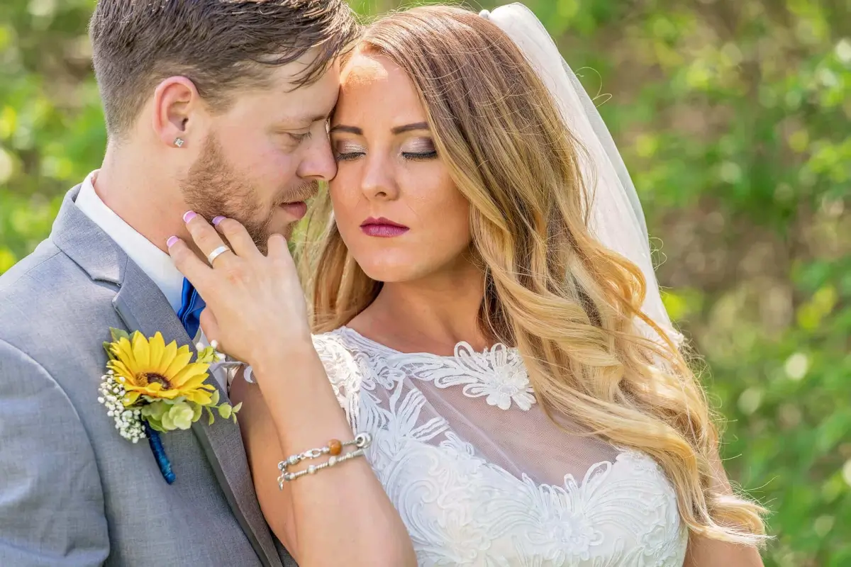 Bride and groom close-up portrait with bride resting head against groom's forehead, groom wearing sunflower boutonniere, wedding portrait