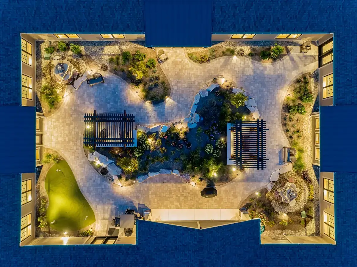 Top-down aerial drone view of a landscaped courtyard with pergolas and putting green lit at night