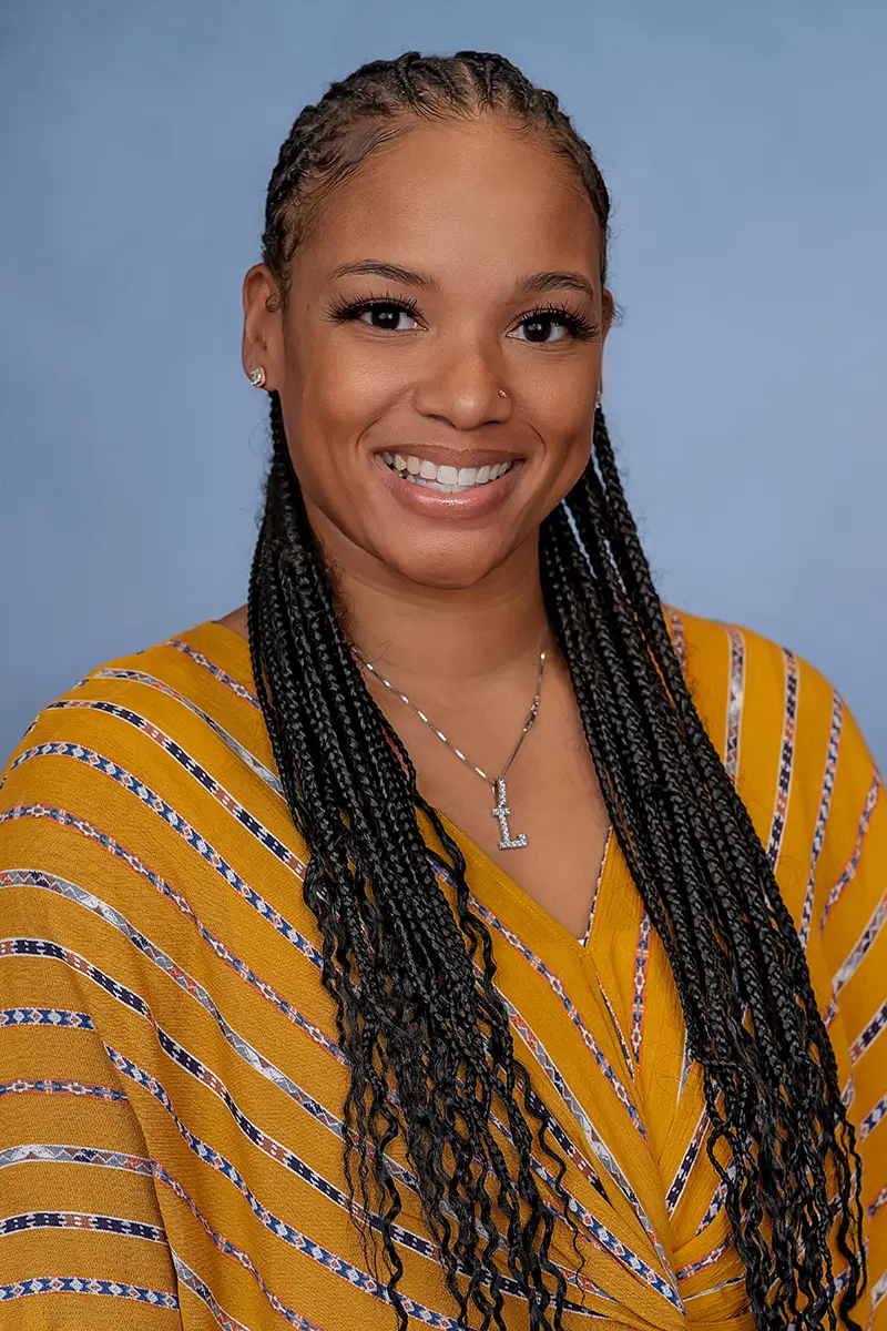 Professional studio headshot of smiling woman in yellow top on light blue background