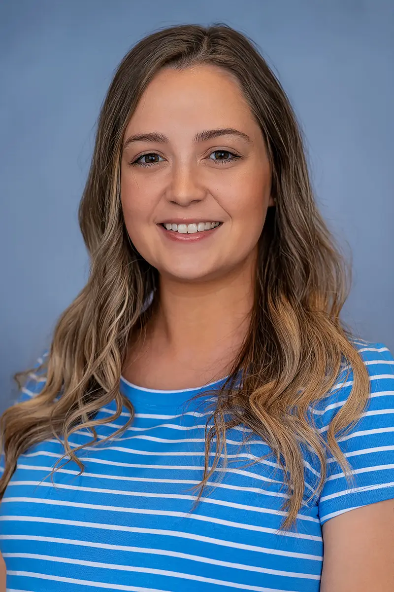 Professional studio headshot of smiling woman in blue striped top on light blue background
