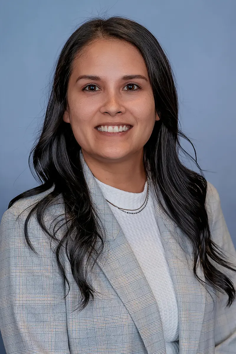 Professional studio headshot of businesswoman in plaid blazer on light blue background