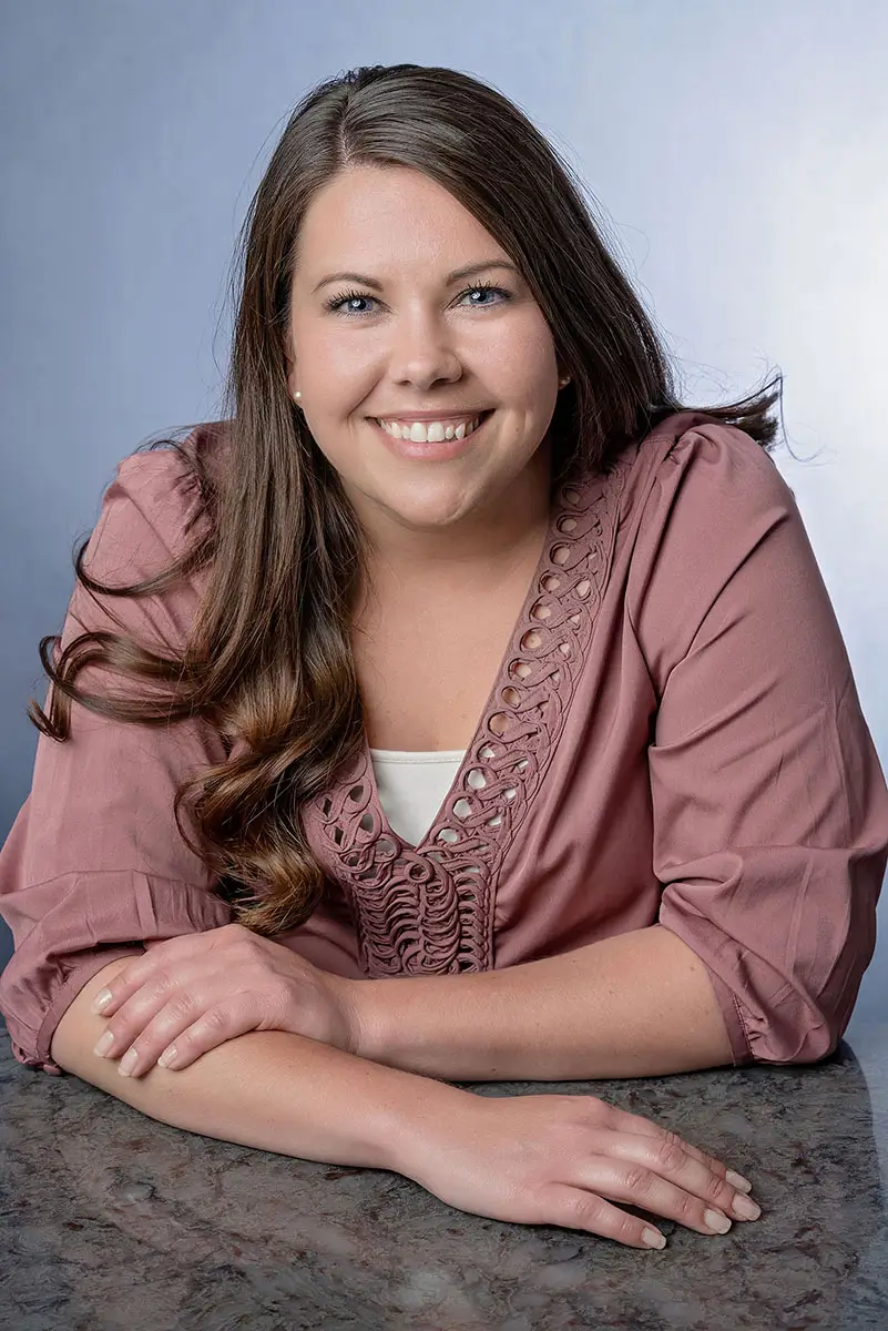 Professional studio portrait of smiling woman in mauve blouse at granite countertop