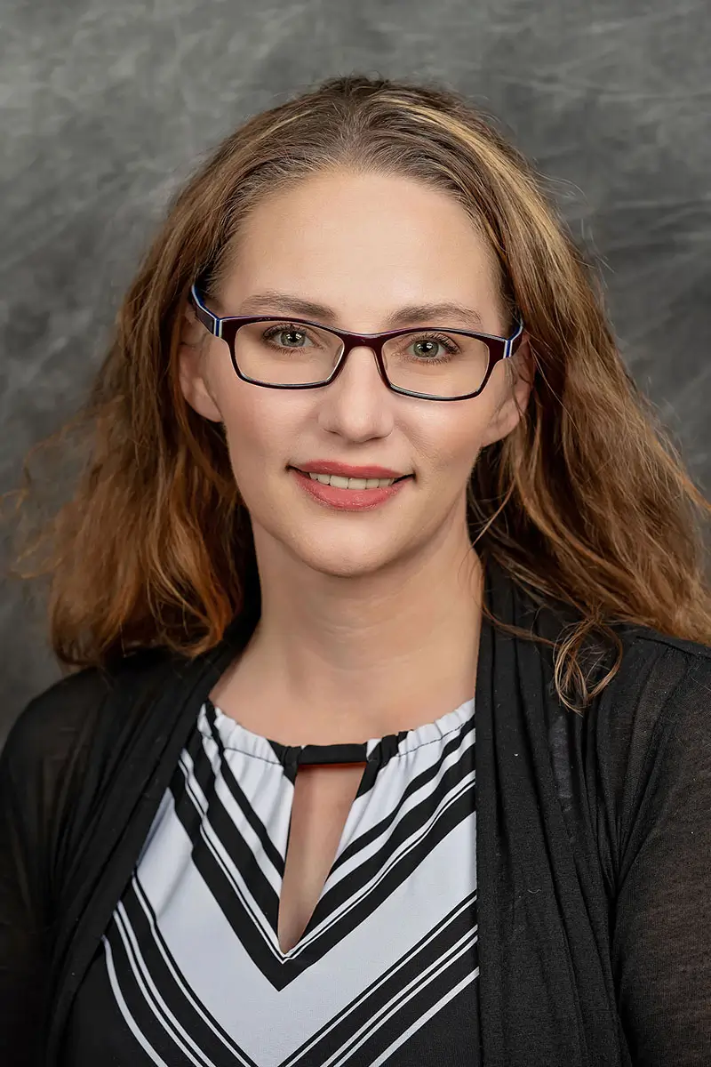 Professional studio headshot of woman with glasses in black cardigan on gray textured background