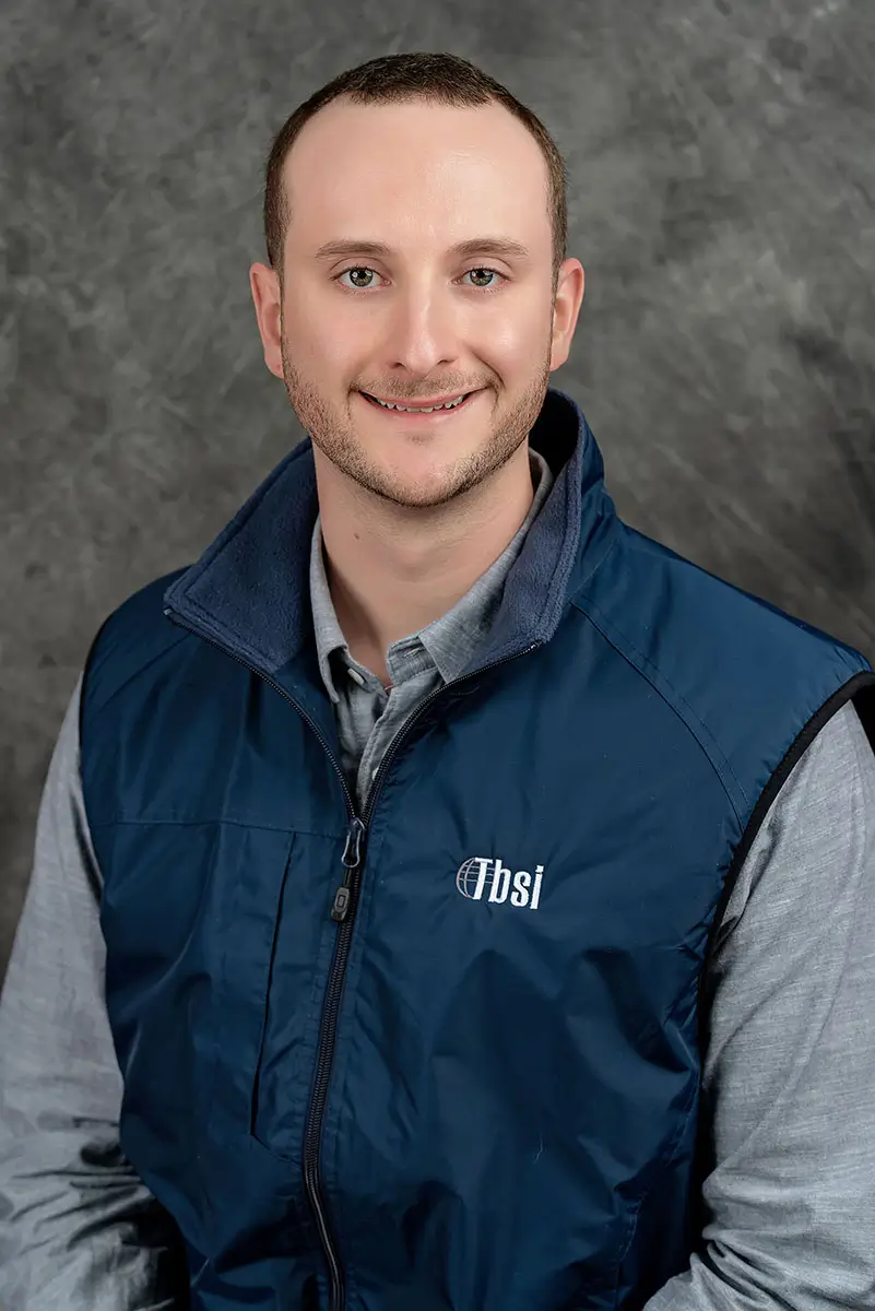 Professional studio headshot of man in navy company vest on gray textured background